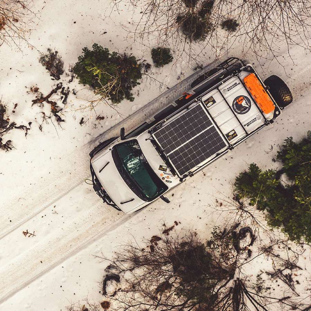 A white van with a Go Power! Solar Elite Charging System on its roof parked in a snowy landscape.