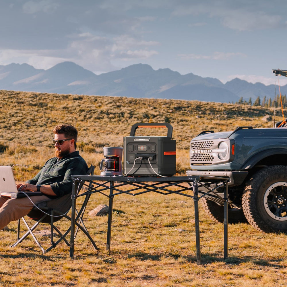 Person using a laptop connecting to Jackery Explorer 1500 Ultra Portable Power Station outdoors with a truck and mountains in the background