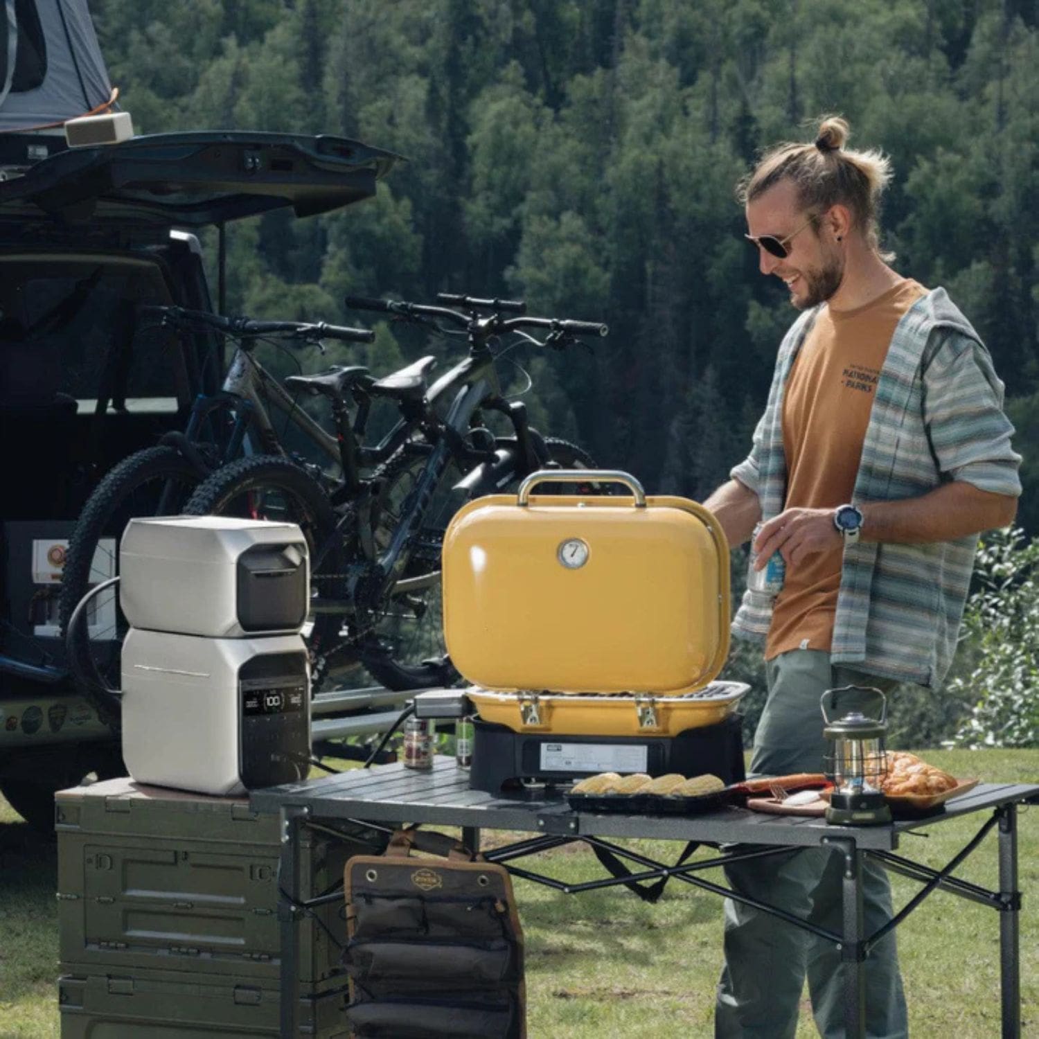 A man grilling outdoors in a mountain setting with EcoFlow DELTA 3 Series Smart Extra Batteries in a portable station powering his equipment