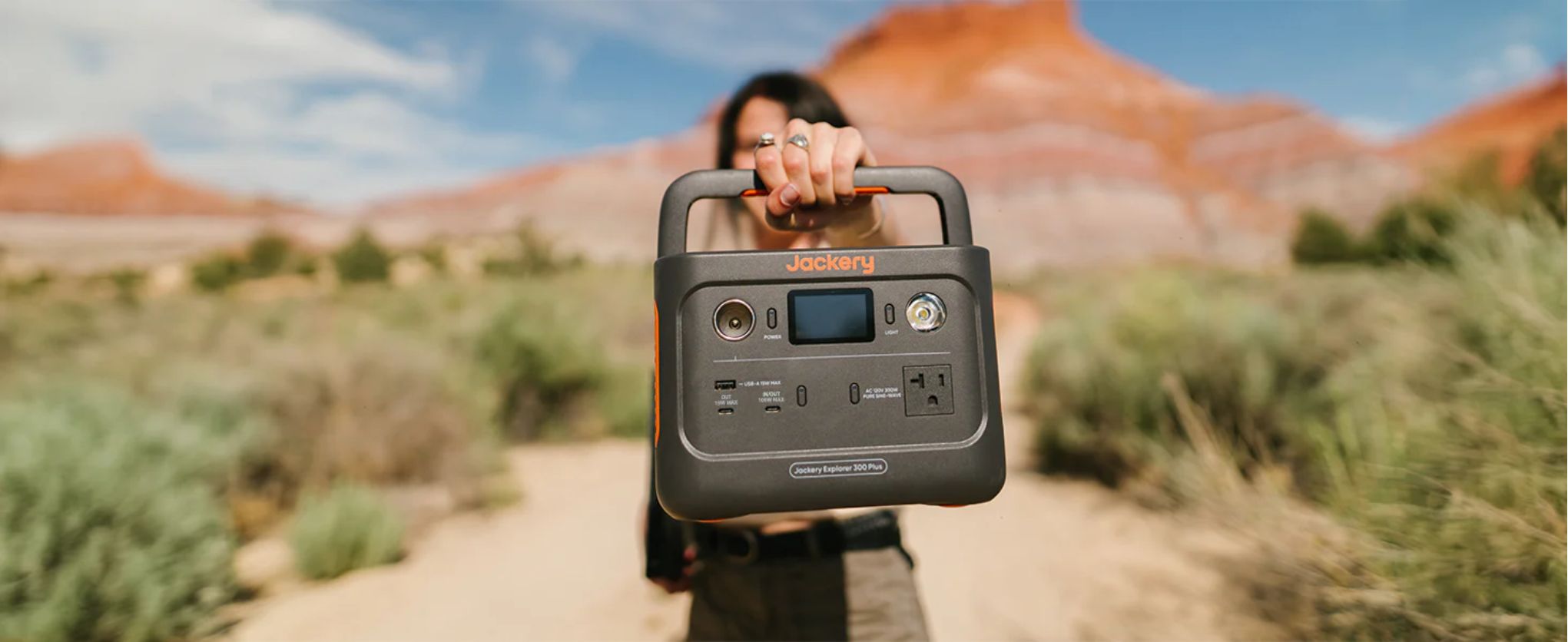 A person holding the Jackery Explorer 300 Plus Portable Power Station in a desert setting