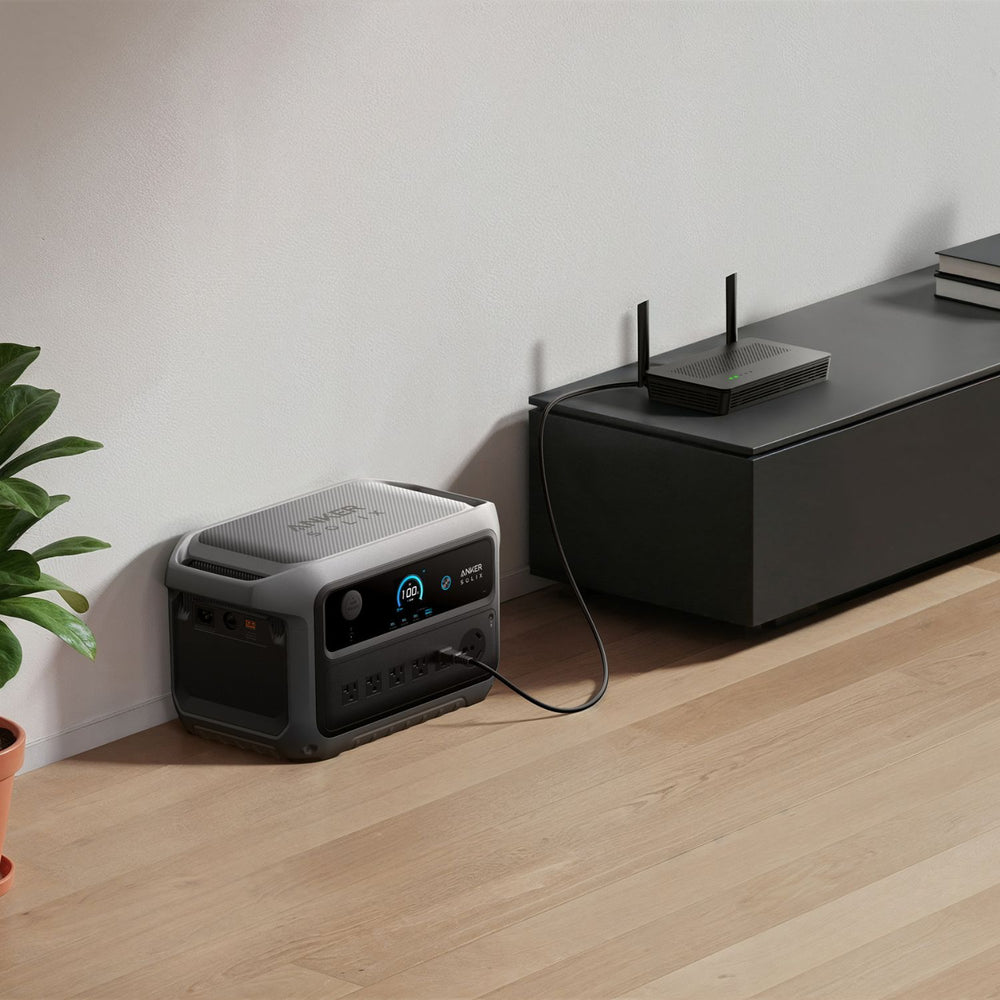 Anker SOLIX C2000 Gen 2 Portable Power Station connected to a router on a wooden floor with a plant nearby.