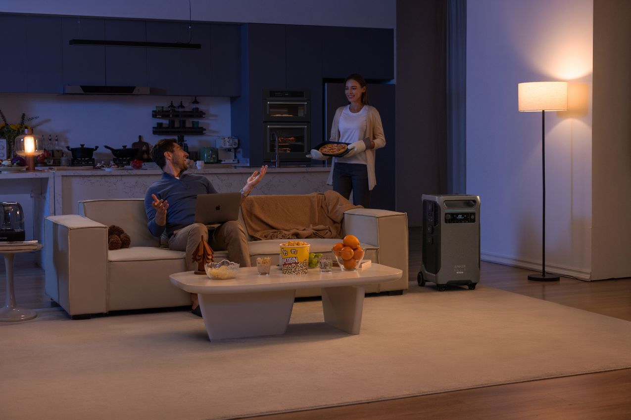 Anker SOLIX F3800 Plus Power Station in the living room with a man using a laptop and a woman holding a pizza