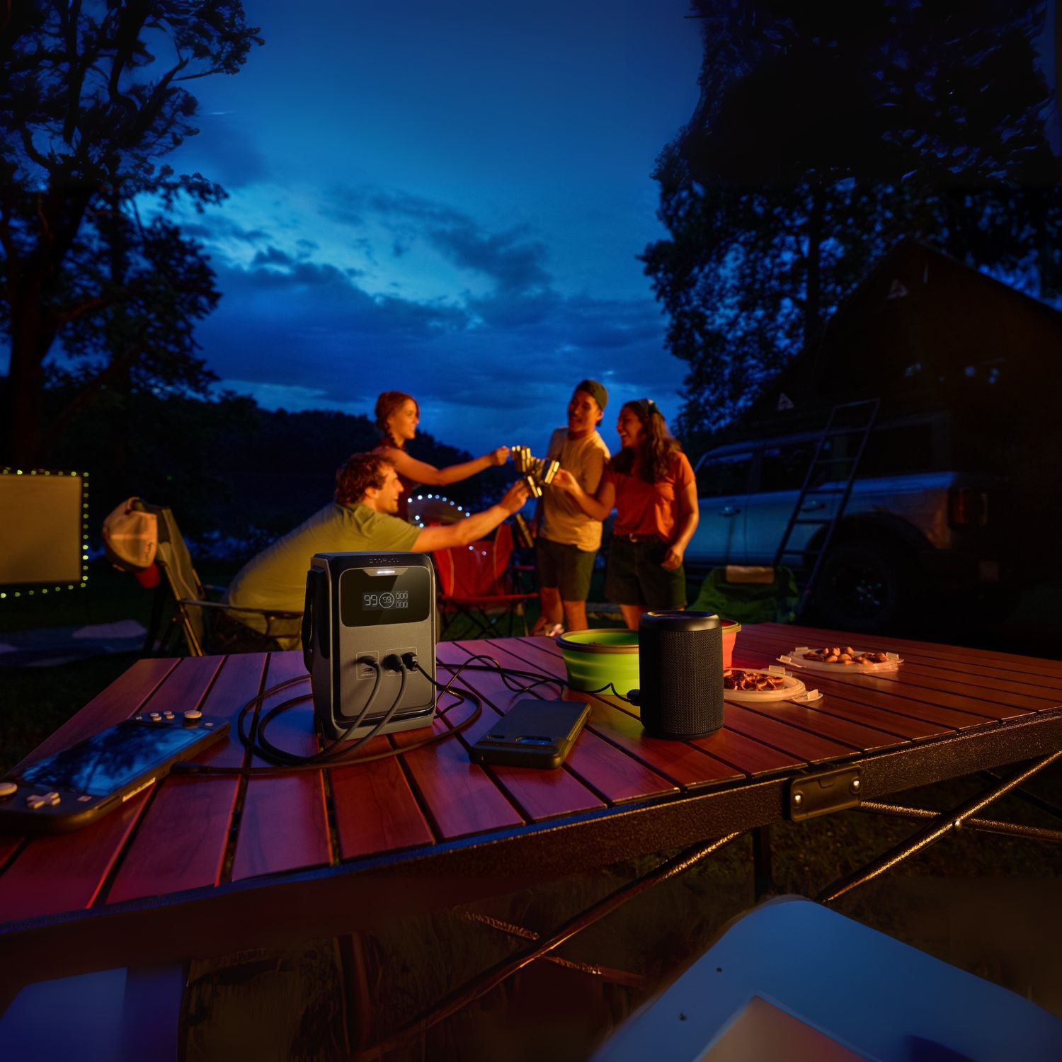 Group of people around a picnic table at night with a EcoFlow TRAIL 200DC Portable Power Station and speakers.