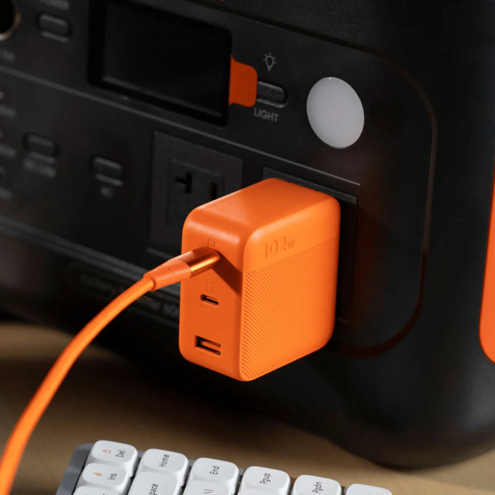 Jackery 102W GaN 3-Port Fast Charger plugged into a black power station with a keyboard in the foreground.