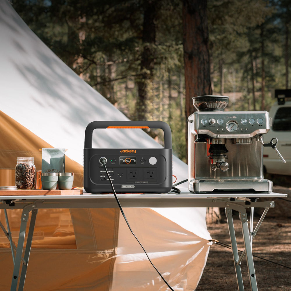Jackery Explorer 600 v2 next to a coffee machine on a camping table with a tent in the background.