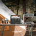 Jackery Explorer 600 v2 next to a coffee machine on a camping table with a tent in the background.