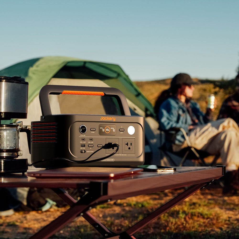 Jackery Explorer 600 v2 on a camping table with a tent and people in the background