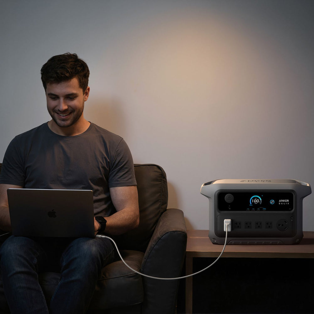 Man using a laptop connected to Anker SOLIX C2000 Gen 2 Portable Power Station in a dimly lit room.