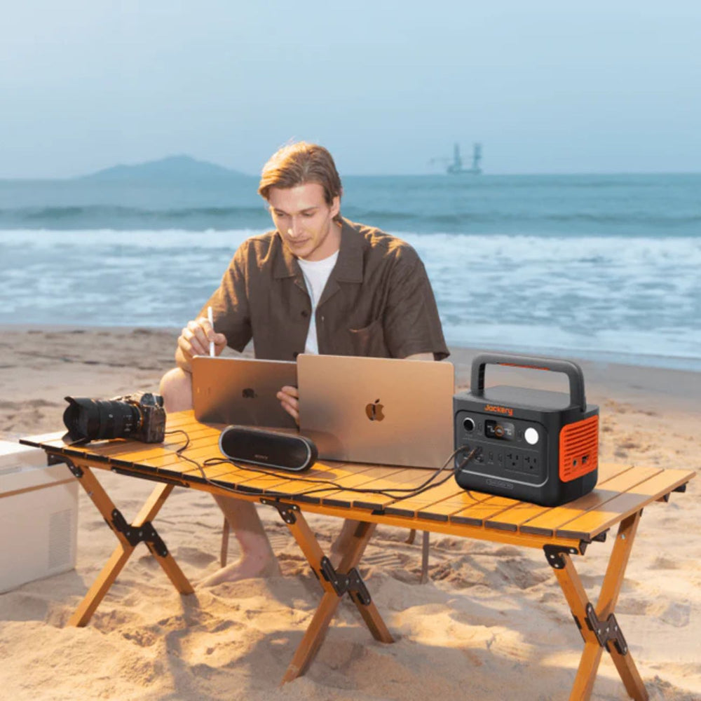 Man using it beside the beach connected to a macbook Jackery Explorer 300 v2 Portable Power Station