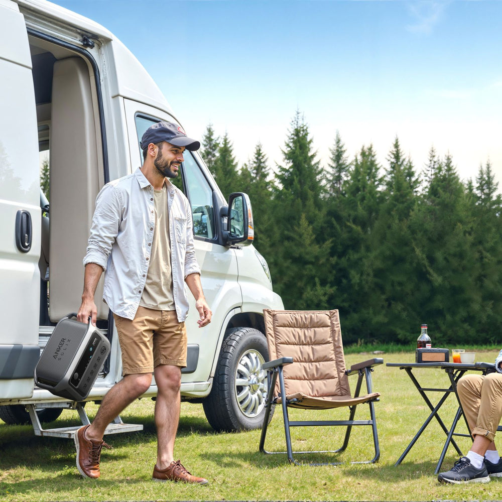 Man walking towards a campervan with outdoor furniture and drinks in a forest setting holding Anker SOLIX C2000 Gen 2 Portable Power Station