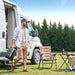 Man walking towards a campervan with outdoor furniture and drinks in a forest setting holding Anker SOLIX C2000 Gen 2 Portable Power Station