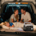 OUKITEL P1000 PLUS Portable Power Station in a car trunk with a family in the background, emphasizing quiet operation.