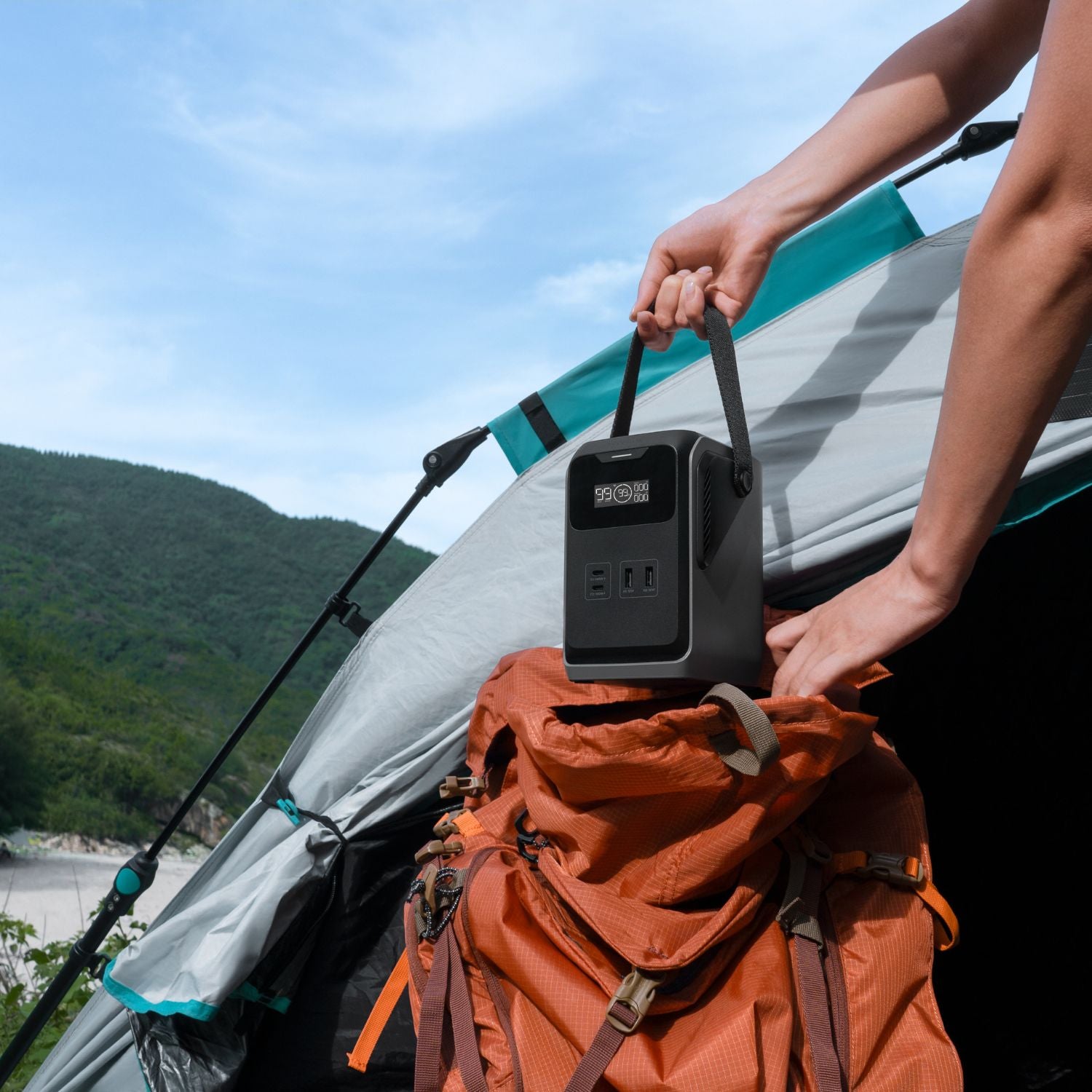 Person attaching a EcoFlow TRAIL 200DC Portable Power Station to an orange backpack outdoors with mountains in the background