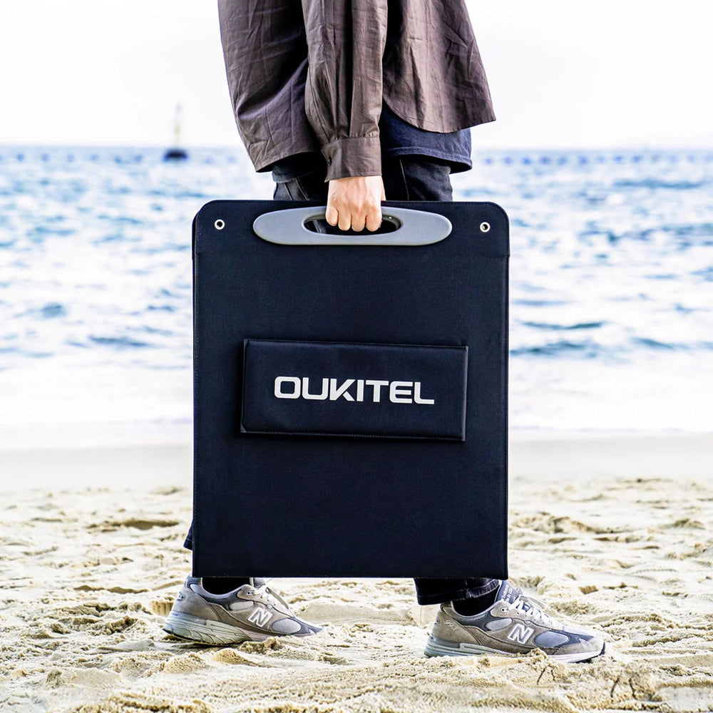 Person holding a OUKITEL 200W Portable Solar Panel on a beach.