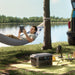 Person in a hammock by a lake using a tablet, with a Anker SOLIX C2000 Gen 2 Portable Power Station on the ground.