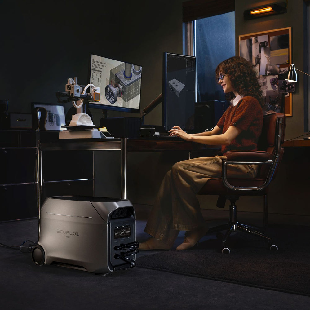 Person sitting at a desk with multiple monitors in a dimly lit room, using a EcoFlow DELTA 3 Ultra Plus Portable Power Station .