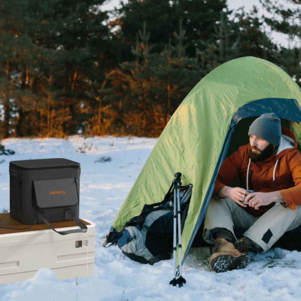 Person sitting inside a green tent in a snowy landscape with a Jackery Extreme Guard Carrying Bag and backpack nearby.