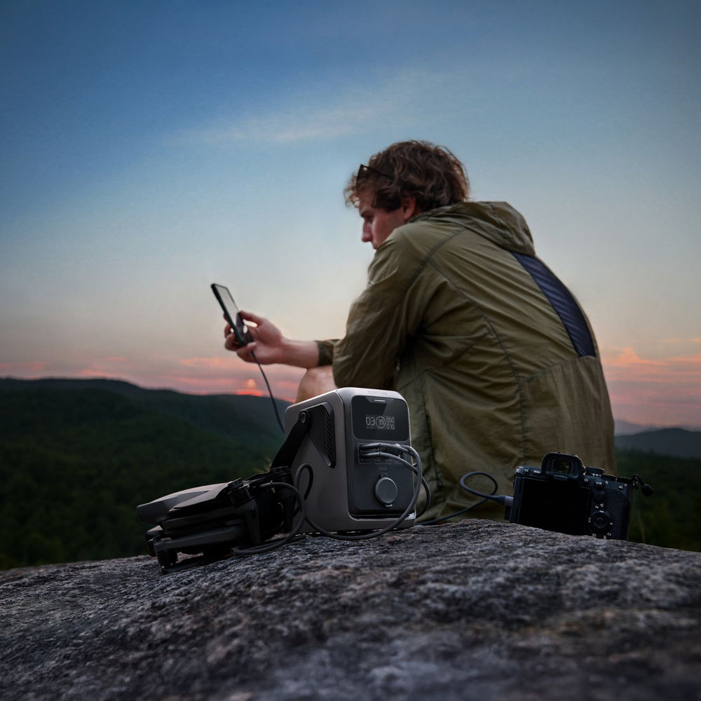 Person sitting on a rock with a backpack and camera charging in Group of people enjoying a campfire at night with a EcoFlow TRAIL 300DC Portable Power Station on a table