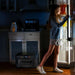 Person standing in a dark kitchen using a BLUETTI Apex 300 Portable Power Station to power a refrigerator.