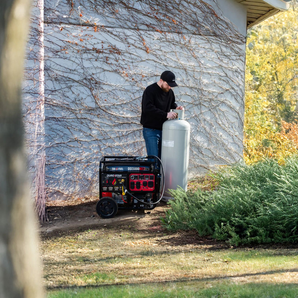 Person using a DuroStar DS13000MXT Tri-Fuel Generator outside a house with trees in the background
