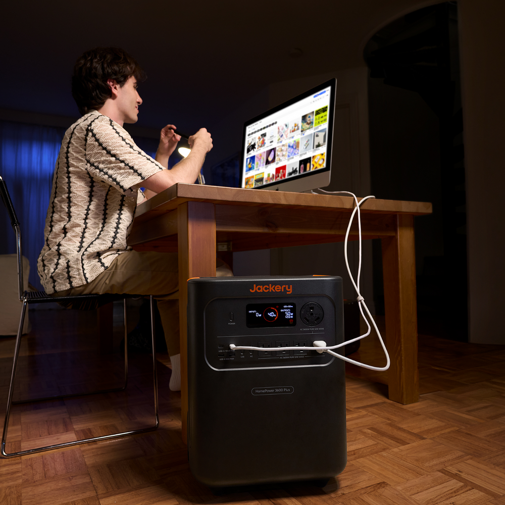 Person using a computer with a Jackery HomePower 3600 Plus Portable Power Station  on a wooden floor.