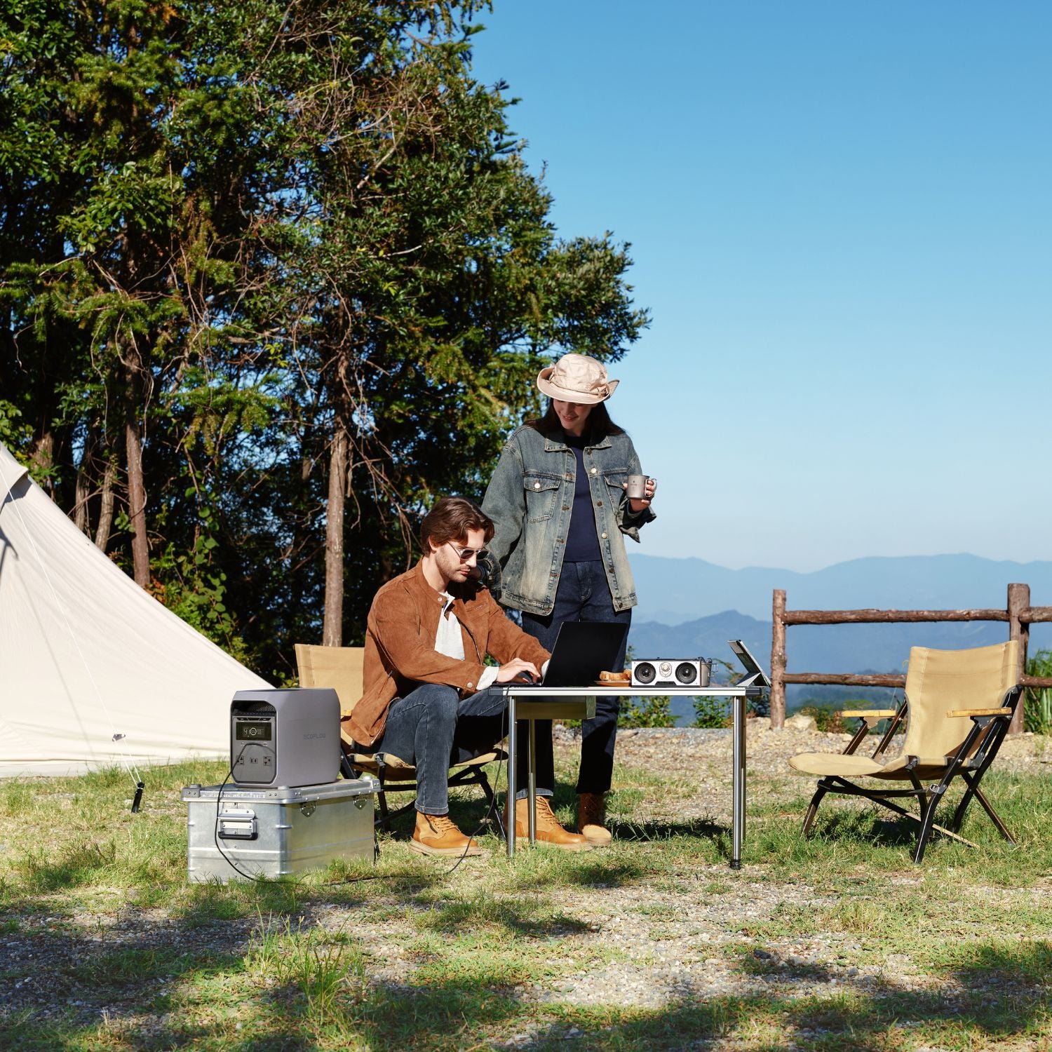 Two people at a campsite with a tent, chairs, and a table under a clear blue sky using a laptop connected to EcoFlow DELTA 3 Classic Portable Power Station