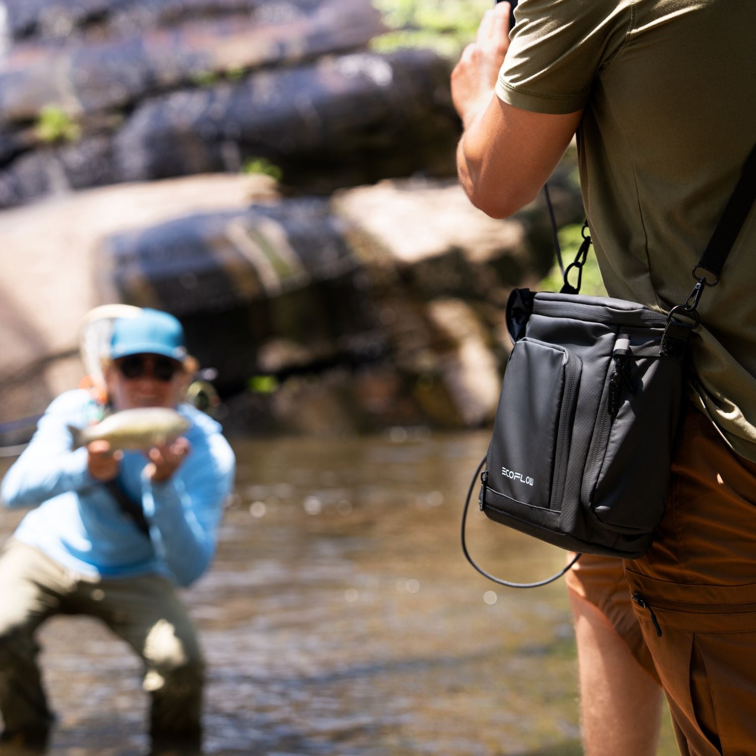 Two people fishing by a river with one person holding a fish and the other wearing EcoFlow TRAIL 200DC Portable Power Station