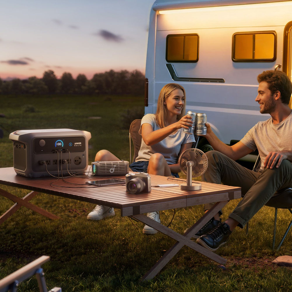 Two people sitting at a table outdoors with a camper van in the background with Anker SOLIX C2000 Gen 2 Portable Power Station in the table