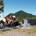 Two people sitting on a blanket outdoors with a solar panel and EcoFlow DELTA 3 Classic Portable Power Station in front of a mountainous landscape.