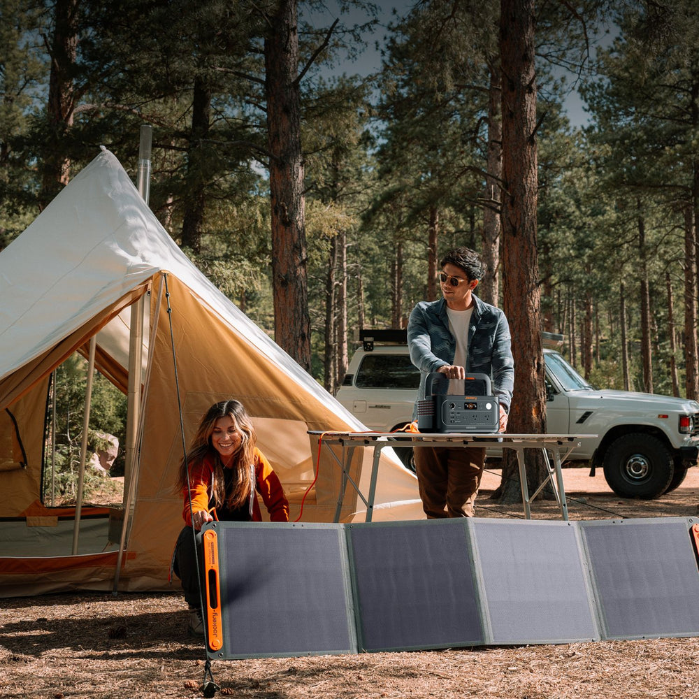 Two people with a tent and solar panel in a forest setting connected to Jackery Explorer 600 v2