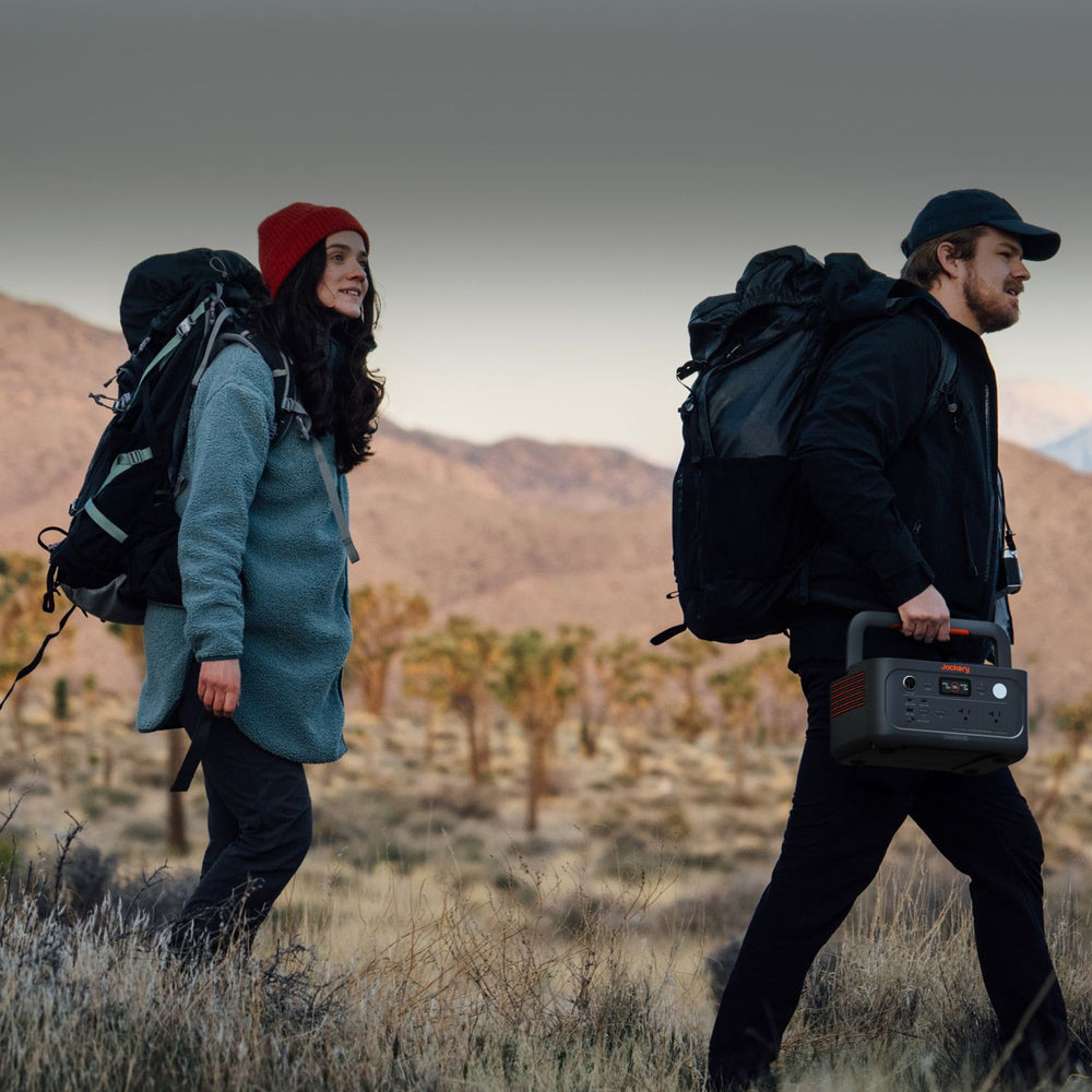 Two people with backpacks walking through a desert landscape holding Jackery Explorer 600 v2
