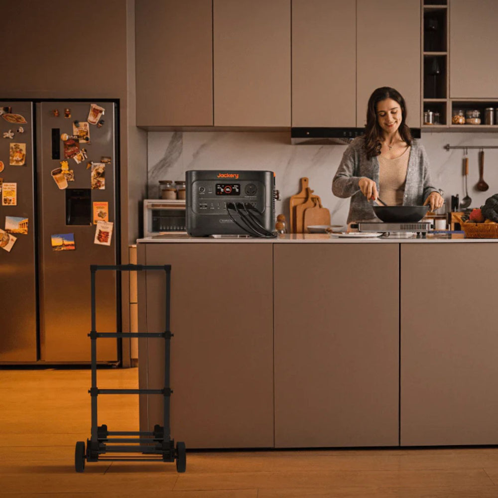 Woman cooking in a kitchen with a portable power station on the counter and a Jackery Power Station Trolley beside it