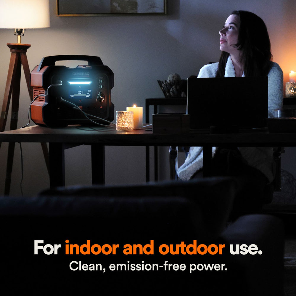 Woman sitting in a dimly lit room with a Generac GB2000 Portable Power Station, surrounded by candles.