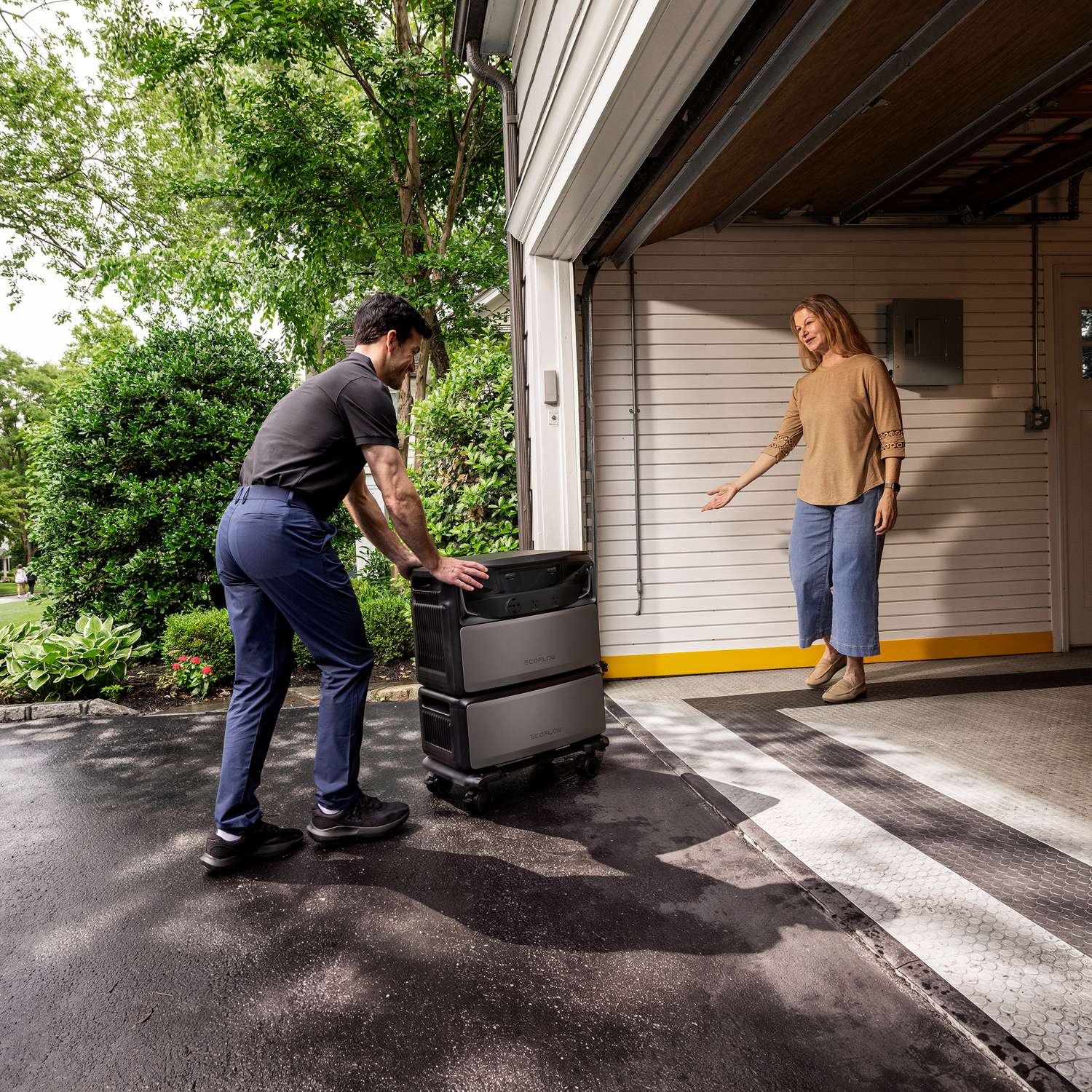 Installer rolling an EcoFlow TITAN 5000 Plus battery stack up the driveway toward the garage