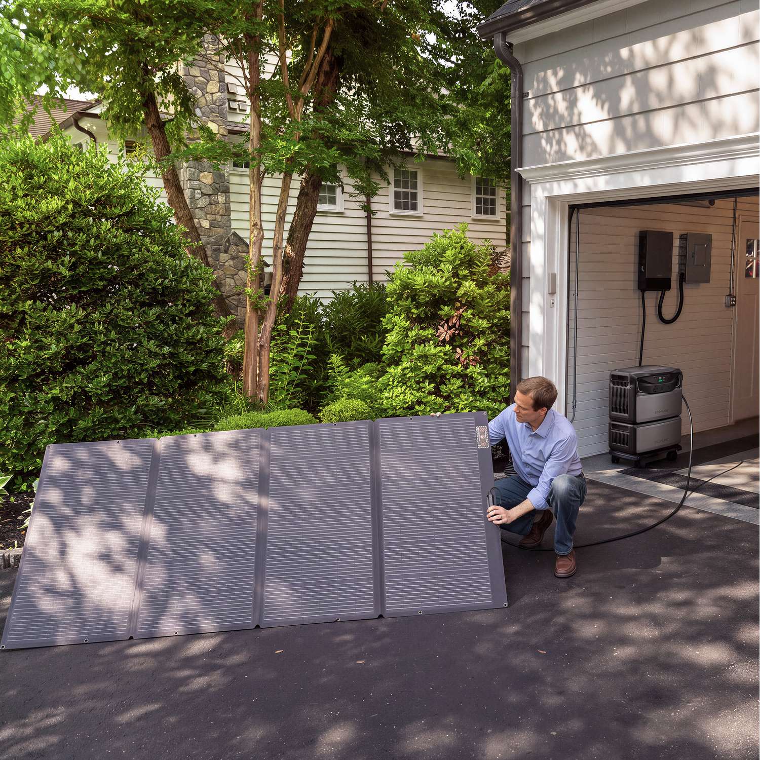 Homeowner on a driveway connecting a folding portable solar panel to an EcoFlow TITAN in the garage