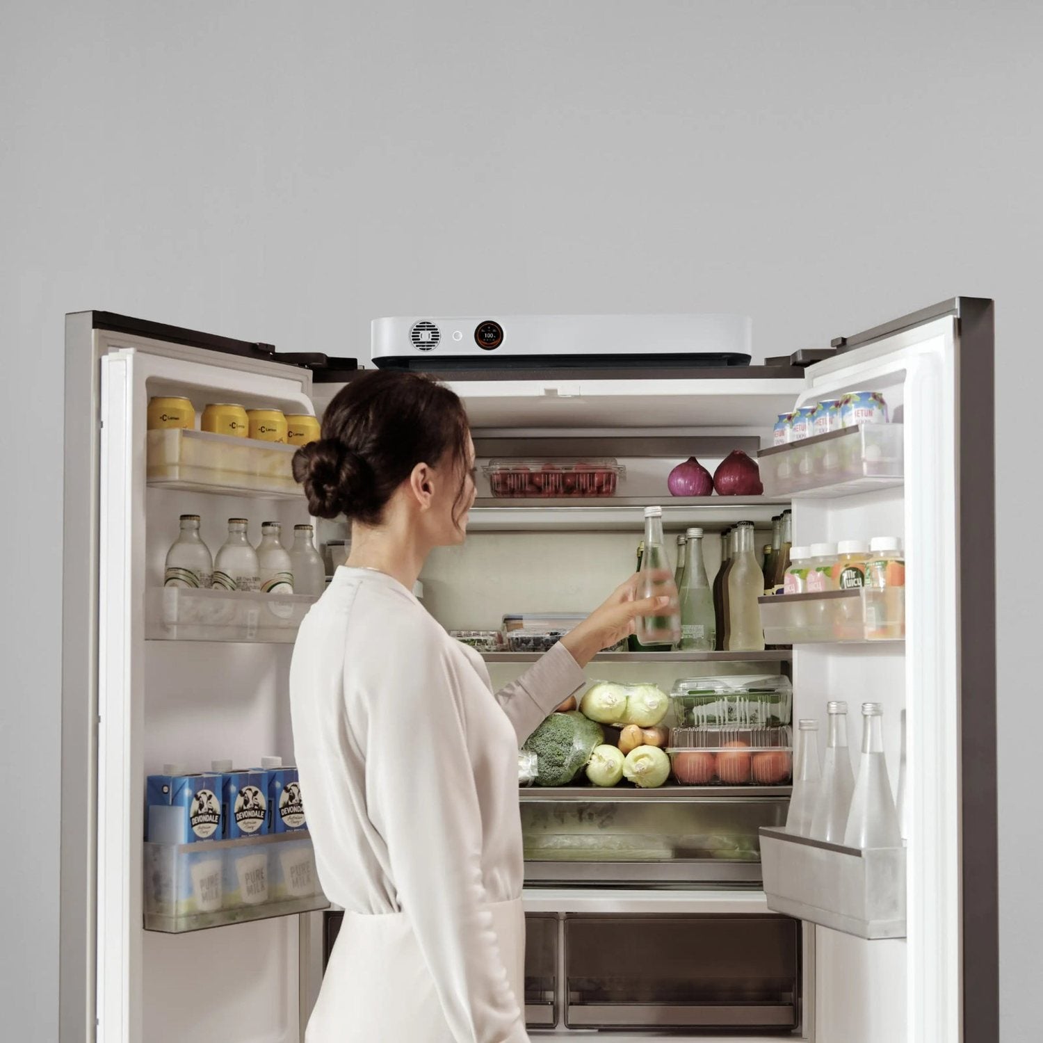 Woman reaching into a refrigerator with a Jackery FridgeGuard on top of the fridge